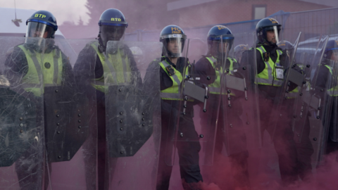 Police officers stood with shields surrounded by pink dust amid clashes with protesters