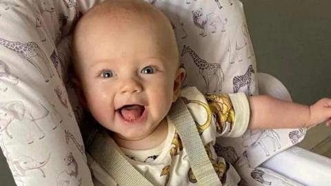 A baby sat in a chair. The baby is smiling.