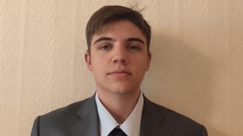 Yaroslav poses for the picture. he is in a shirt, tie and blazer. It is a close up of his head and shoulders. He has brown hair