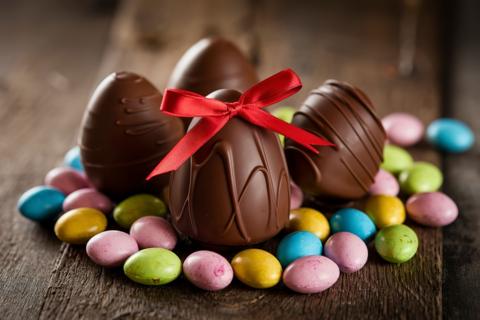Four chocolate eggs surrounded by smaller brightly coloured eggs on a wooden table.