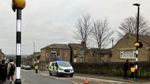 A road in Huddersfield with a police van parked on the right of the image