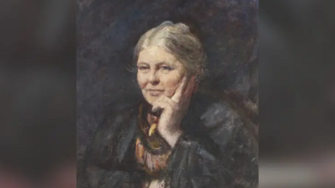 Portrait in oils dating from the turn of the 20th Century of an elderly woman. She appears to be seated and is holding her chin in her left hand. Her hair is grey and she is wearing a dark grey coat over a dress in muted shades of brown, orange and maroon.