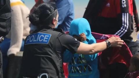 A police woman is helping some young asylum seekers, who are wearing hoodies