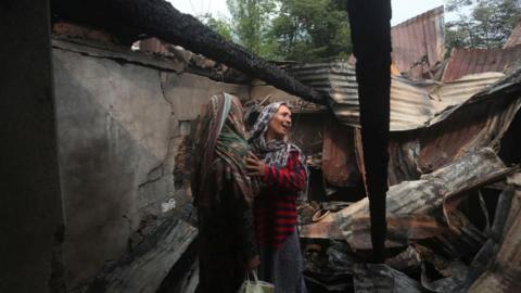 Women hold one another as they stand among debris