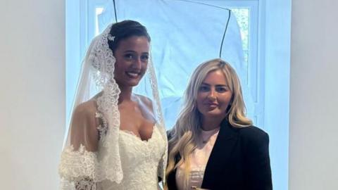 Venezuela Fury in a wedding dress stood next to Lynsey Austin. She is wearing a black jacket and a pink top underneath it.