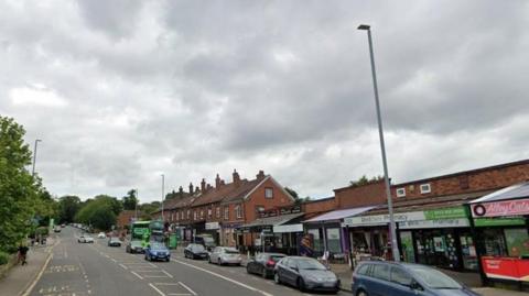 A main road with a parade of shops and cars parked on the roadside.