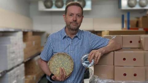 Simon Spurrell stood holding a wheel of blue cheese