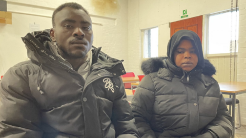 Man and his wife dressed in black winter coats looking serious