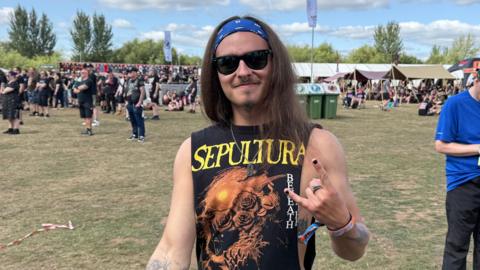 Man with long brown hair wearing rock music vest and sunglasses