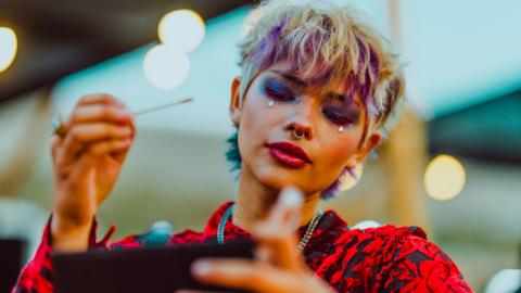 A woman applying bright make-up at a festival