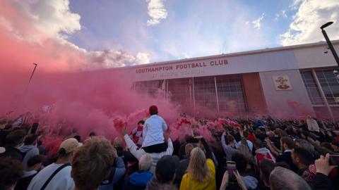 fans gathered out the front of St Mary's stadium with red flares smoking.