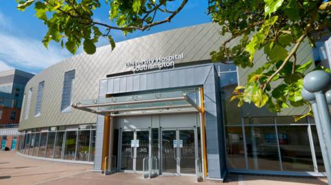 The front of a large, modern-looking building has a sign on the front which reads University Hospital Southampton. 