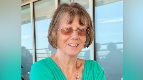 Christine Murton is in the middle of the image looking towards the camera. She has short brown hair and is wearing glasses and a green T-shirt.