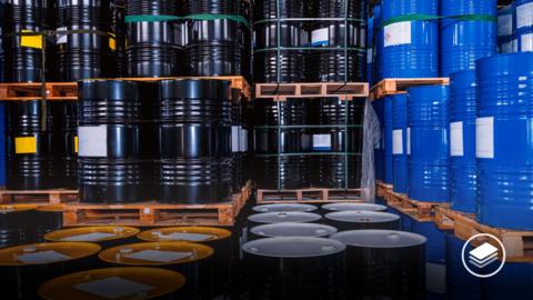 A chemical plant warehouse full of colourful large blue and black barrels.