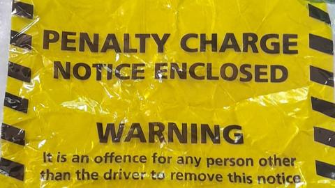 A yellow and black parking ticket which says PENALTY CHARGE NOTICE ENCLOSED.