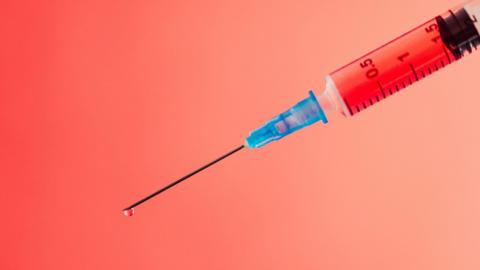 Stock image of needle with red liquid in it. The background of the needle is red tinted.