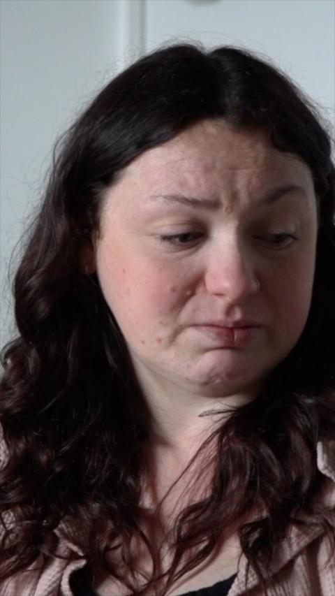 A woman with long brown hair looks away from the camera and is upset.