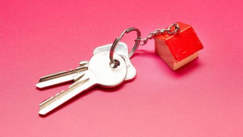 A set of house keys with a house shaped fob on a pink surface.