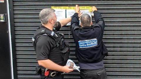 Members of Nottingham Trading Standards and Nottinghamshire Police place closure orders on a black shuttered shop