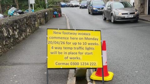 A temporary yellow road sign in Newlyn is in the road informing motorists that 4 way traffic lights will be in place for 10 weeks 
