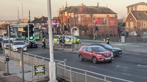 Police officers and a police van at the scene on York Road. There are two cars stopped in the middle of the road, one with a dent in the bonnet. Behind the police are cars and buses. 