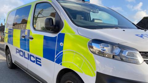 A picture of the side of a police van. It is green, blue and white in colour. It has the word 'POLICE' on the side of it.