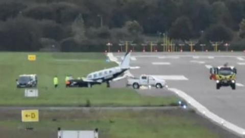 A light aircraft on a field next to a runway surrounded by cars