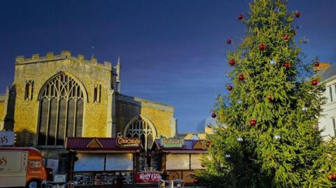 A Christmas tree with red decorations set in front of a church and food carts 