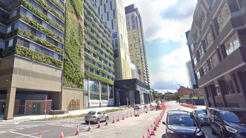 A Google Maps image of Victoria Way in Woking. There is a large hotel to the left of the road and a number of cars driving on the road. 