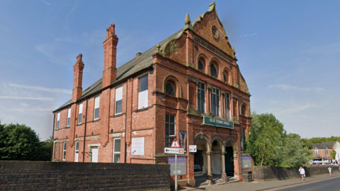 A large red-brick gabled building with pillars at the entrance