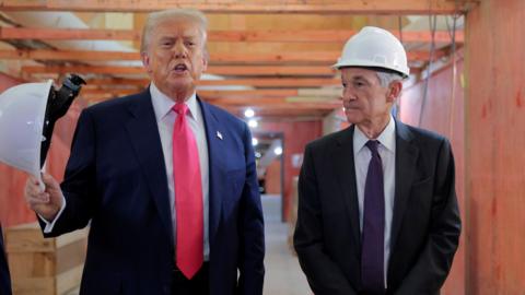 U.S. President Donald Trump waves a hard hat and Federal Reserve Chair Jerome Powell looks to the side while touring the Federal Reserve’s $2.5 billion headquarters renovation project on July 24, 2025 in Washington, DC. 