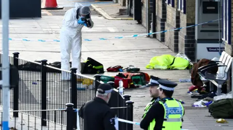Emergency services dressed in black stand on a platform next to a train