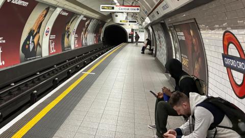 People wait on a Tube platform at Oxford Circus waiting for a train