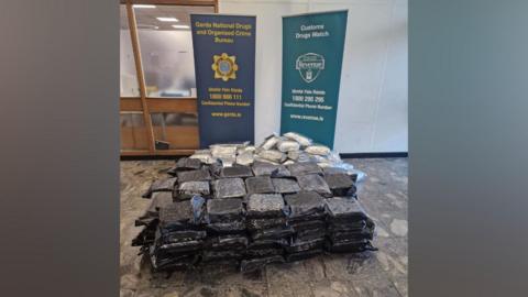 A large quantity of packets of cannabis on a floor with Gardaí signs behind it.