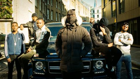 A street gang stand around a car