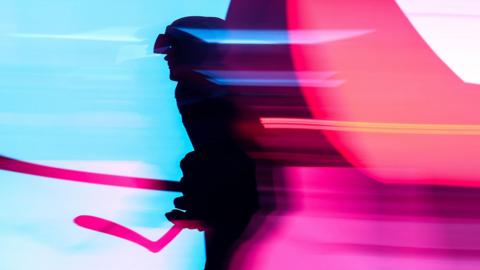Silhouette of an ice hockey athlete, shown in motion blur against a vivid background of blue and pink light streaks, creating a dynamic, futuristic atmosphere with strong contrast and abstract shapes.