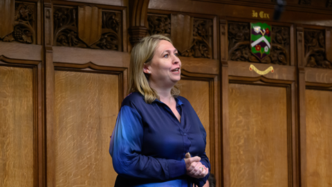 MP Karen Bradley standing up in the House of Commons. She is wearing a blue dress and there is wood panelling in the background