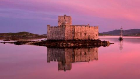 Kisimul Castle and yacht in a pink sunset