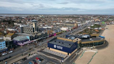 A drone shot of Marine Parade in Great Yarmouth looking north along the beach, with a tower, leisure centre and seafront arcades in view on a cloudy day.