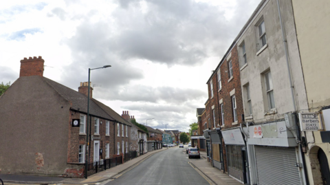 Wellowgate in Grimsby. Building line either side of the empty street and there is a silver coloured car parked on the right