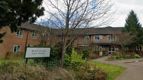 A sign for Beechwood Care Home in Northallerton with the care home building in the background. There are multiple trees around the site.