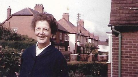 An old photo of an older woman smiling outside a house