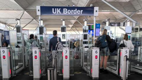 Queue of people waiting to pass UK border checks at an airport in London at passport scanners