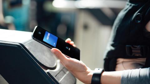 A person paying at a ticket barrier using a phone.