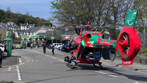 Welsh Air Ambulance is parked on a road. Two police officers are walking on the road.