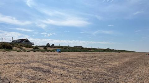 Bright blue sky above sand dunes peppered with mahram grass and a shingle beach at Heacham in Norfolk