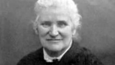 A black and white picture of Mary Higgs. She is starring directly at the camera and smiling