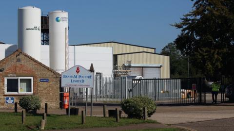 The entrance to the Banham Poultry factory, showing gates, a warehouse and two silos