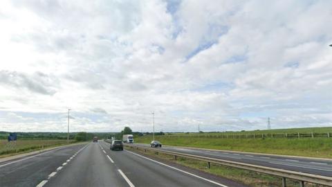 Google Street View of the A1 in Lincolnshire. It is a dual carriageway surrounded by green fields with vehicles driving along it 