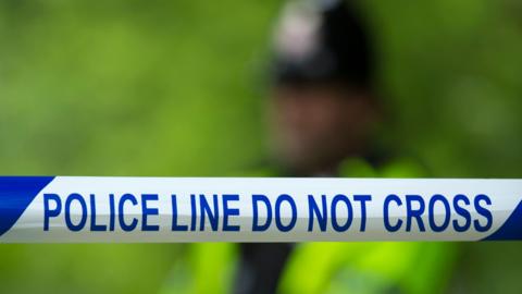 A general view of a police cordon, with the words 'police line do not cross', with an officer in high vis clothing, blurred out in the background